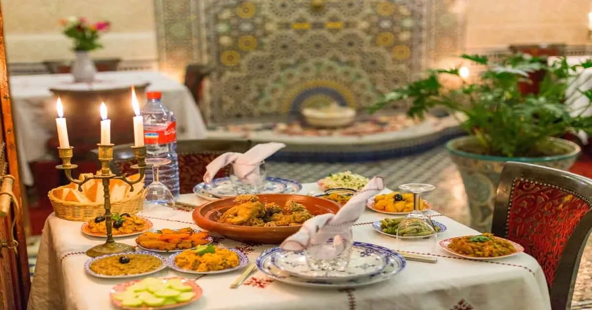 Interior of Moroccan café decorated for Ramadan, colorful hanging lanterns, warm late-day atmosphere, tables prepared for Iftar
